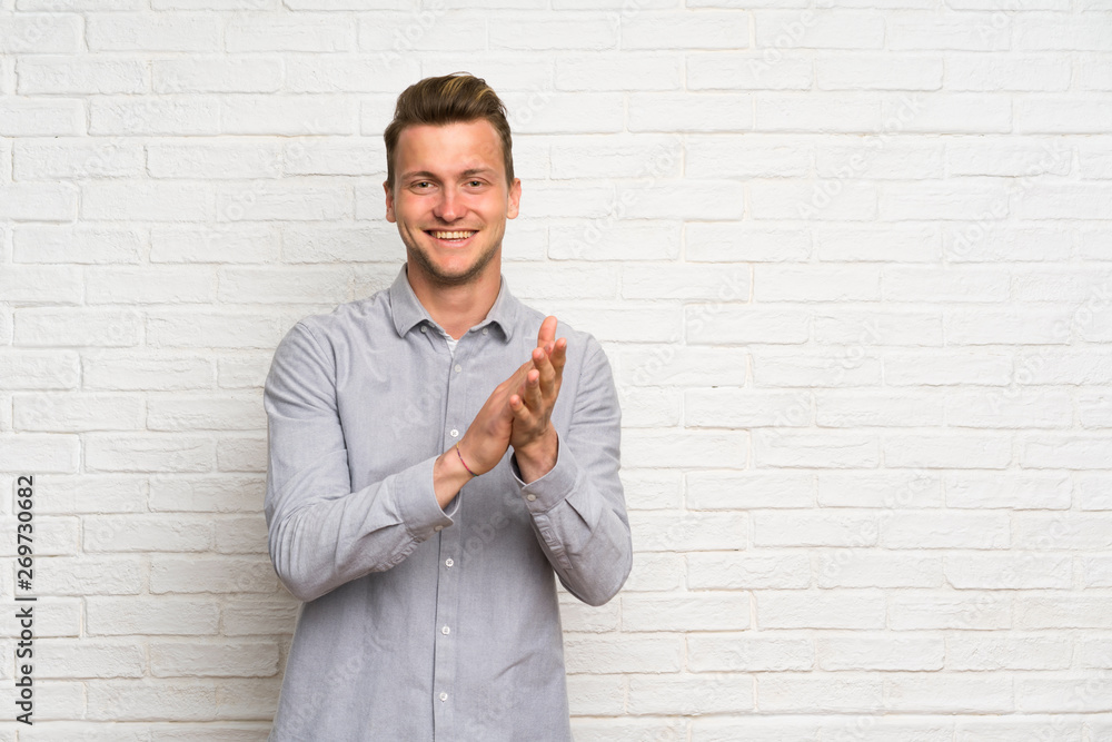 Blonde man over white brick wall applauding after presentation in a conference Blonde man over white brick wall applauding after presentation in a conference