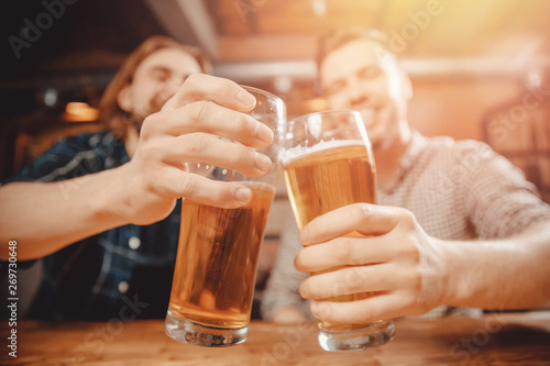 Two cheerful friends sit in sports bar and clink glasses with beer. Friendship concept, hockey fans
