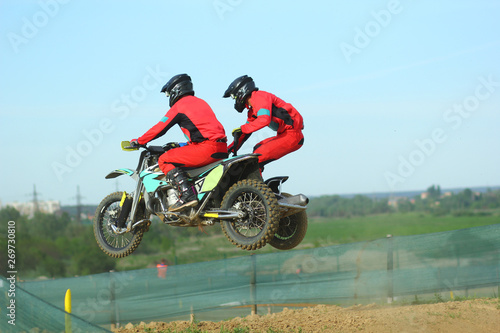 Sidecar motocross athletes jumping on the dirt track 