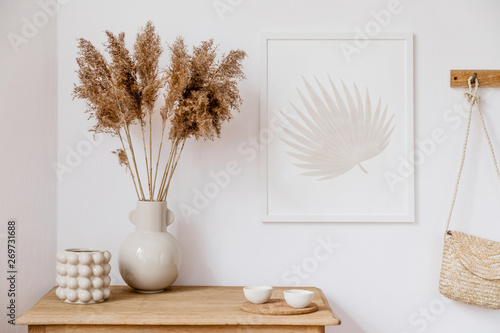 Stylish korean interior of living room with brown mock up poster frame, elegant accessories, flowers in vase, wooden shelf and hanging rattan bag. Minimalistic concept of home decor. Template. Decor.