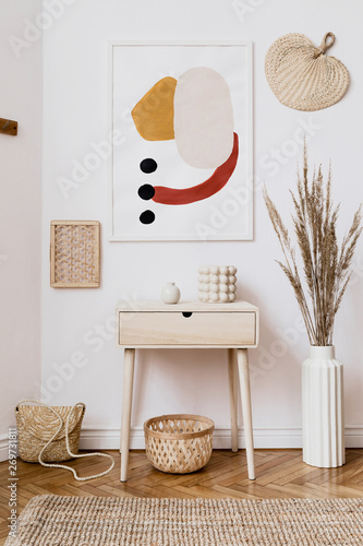 Stylish white interior of living room with mock up poster frame, rattan accessories, leaf, wooden shelf, vase with flowers and elegant personal stuff. Minimalistic concept of home decor. Template. 