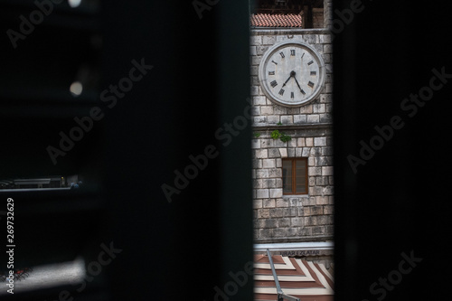 Part of a clock tower in Kotor, Montenegro, shot through half-open window shutters.