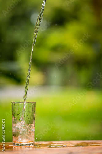 Pouring water from bottle on glass in the public park background. © Watchara