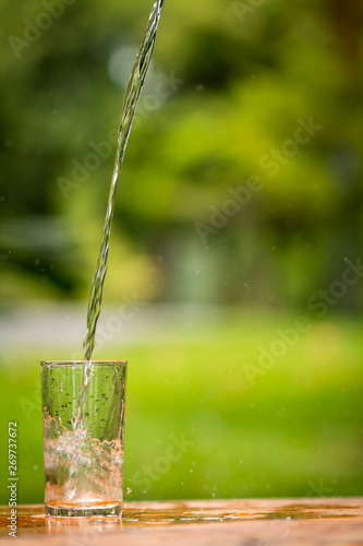 Pouring water from bottle on glass in the public park background.