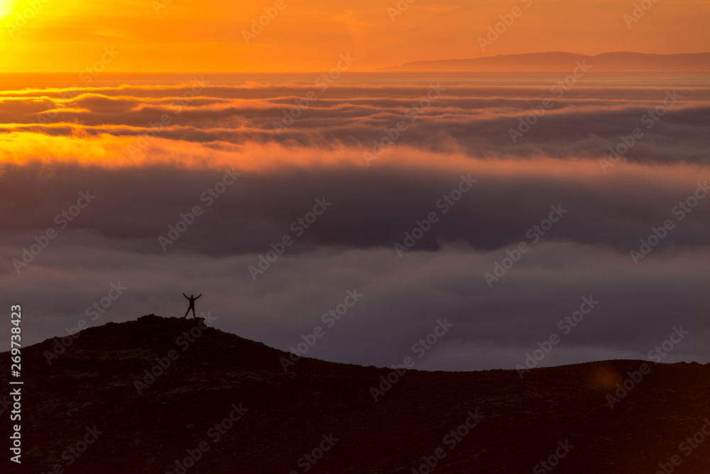 Silhouette of a man on the ridge above the sea of clouds, misty mountains at sunset in Iceland Silhouette of a man on the ridge above the sea of clouds, misty mountains at sunset in Iceland