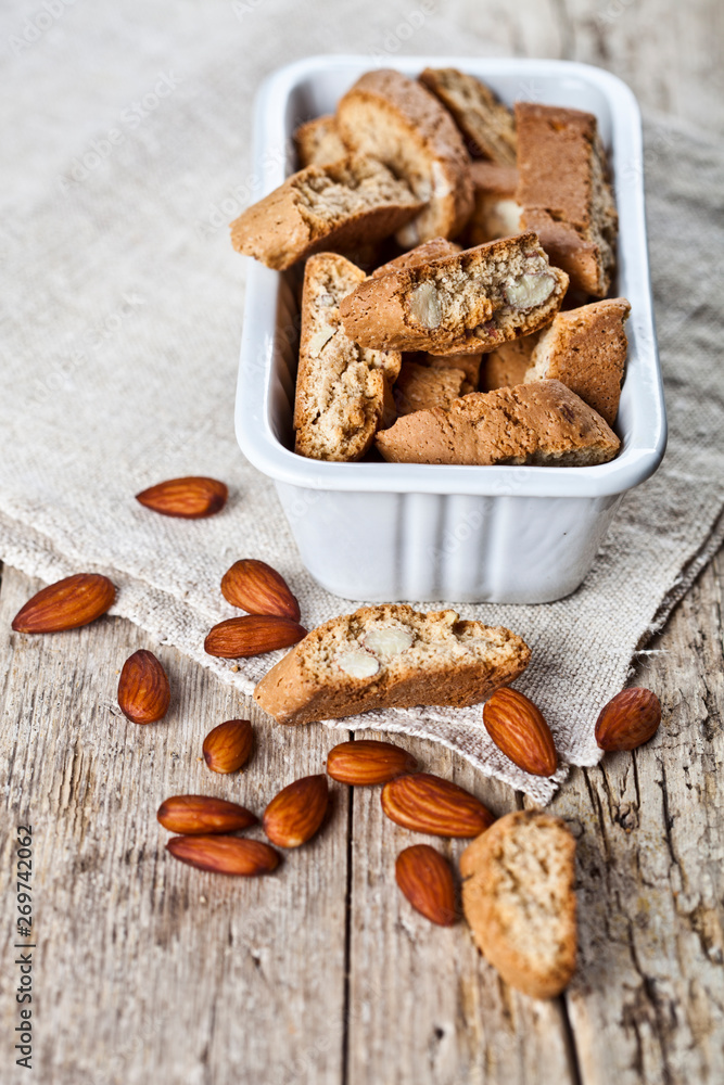 Fototapeta premium Cookies cantuccini in white ceramic bowl and almond seeds on linen napkin closeup on ructic wooden table background.