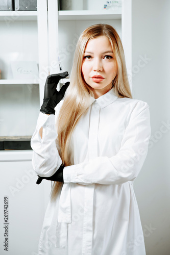 Doctor in pink gown and gloves holds syringe in medical office, ready for making injections. photo