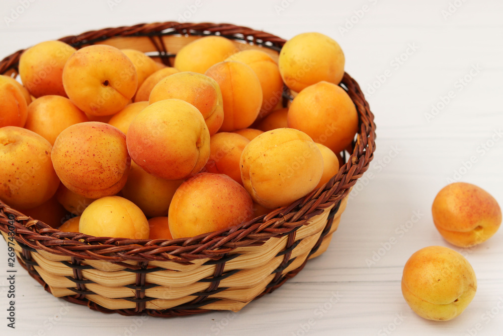 Ripe apricots are located in a wicker basket on a white background