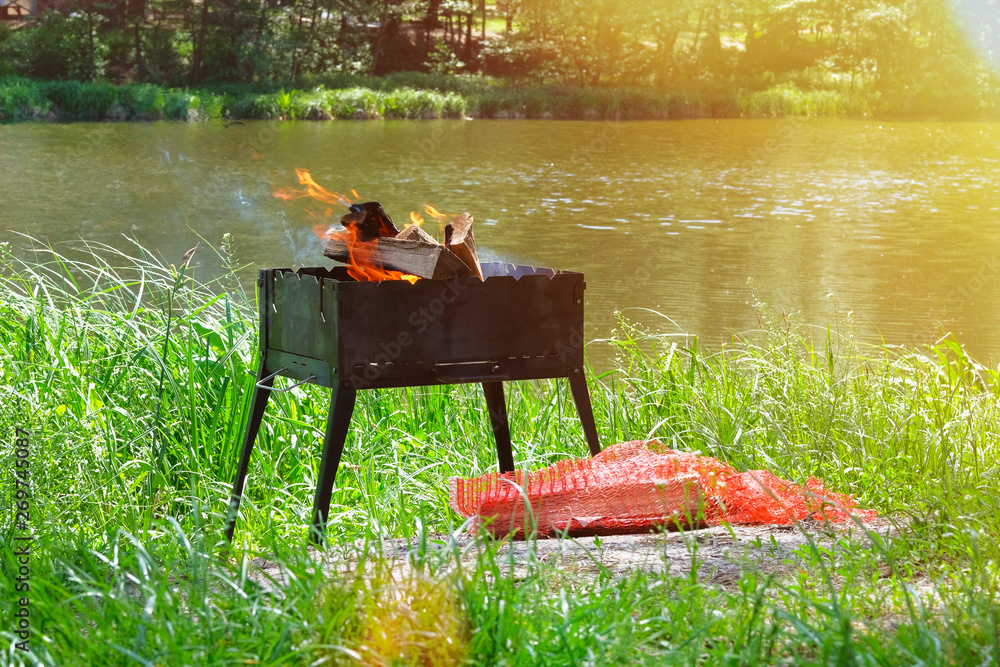 Grill. Picnic. Barbecue on nature. Wood fire prepared for BBQ. Grilling season near water. Sunlight.