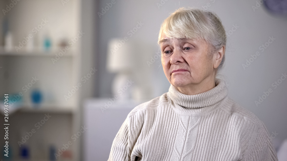 Fototapeta premium Sad elderly woman sitting alone in living room, thinking about health problems