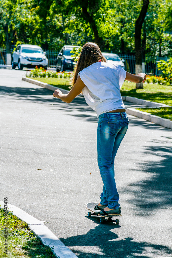 Φωτογραφία girl in a white T-shirt and blue shabby jeans riding a skateboard
