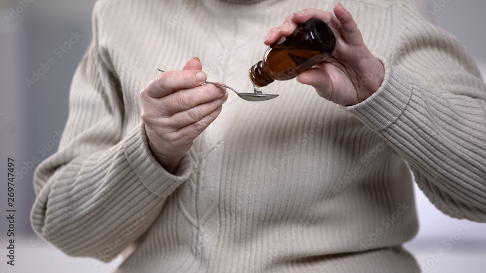 Φωτογραφία Senior woman pouring cough syrup in spoon with trembling hands, health treatment