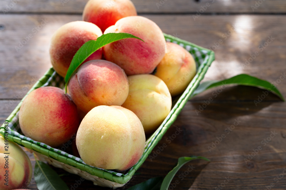 Fresh peaches fruits with leaves in basket on dark wooden rustic background Fresh peaches fruits with leaves in basket on dark wooden rustic background
