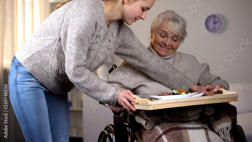 Картината върху платно Female volunteer serving dinner to handicapped old woman, elder care, help