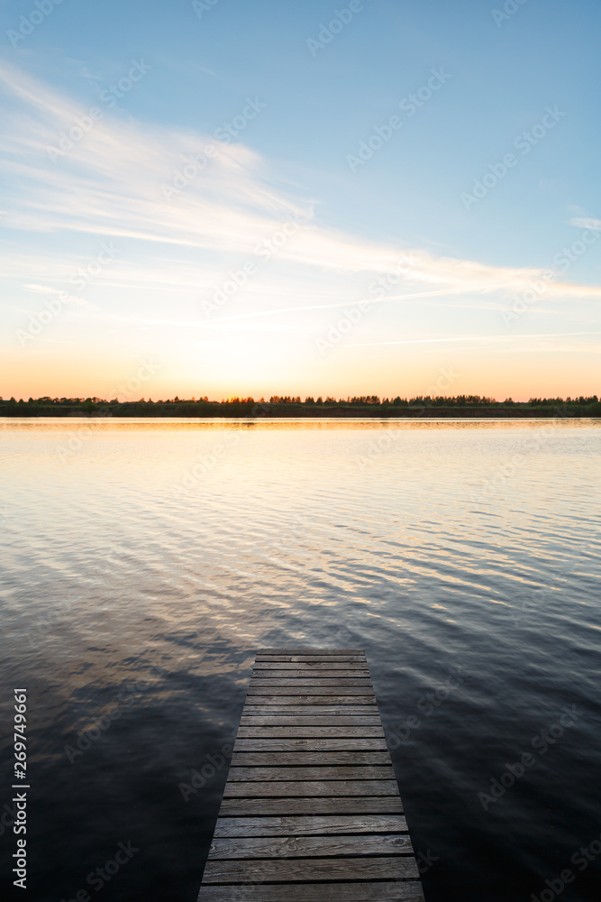 Empty wooden pier on the lake or river. The fisherman is preparing to go to the bridge for fishing. Pier for mooring boats and yachts. Beautiful sunset view
