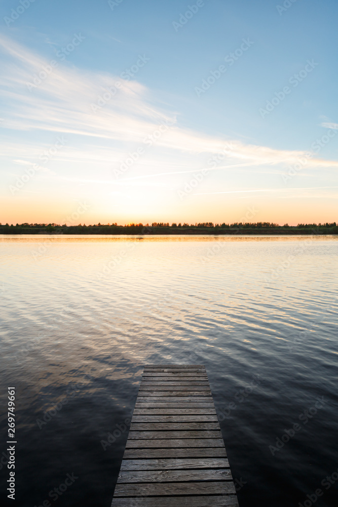 Fototapeta premium Empty wooden pier on the lake or river. The fisherman is preparing to go to the bridge for fishing. Pier for mooring boats and yachts. Beautiful sunset view