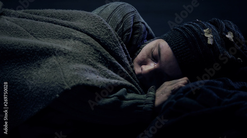 Crying homeless person covered by blanket sleeping on city street, problems © motortion