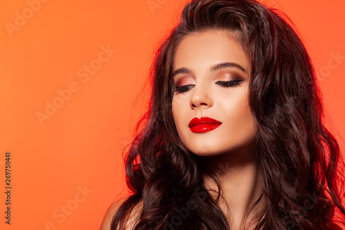 young brunette woman. makeup. Beautiful makeup with red lips, eyes black eyeshadows. space for advertising. orange background. - Image 