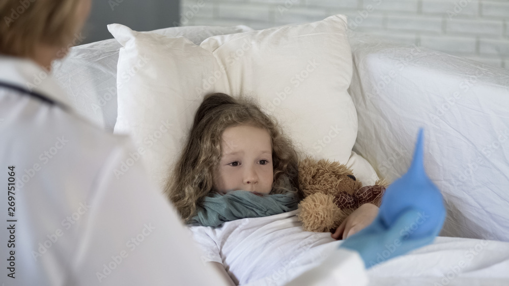 Scared child looking at squeeze bulb in doctors hand with fear in eyes, medicine Scared child looking at squeeze bulb in doctors hand with fear in eyes, medicine
