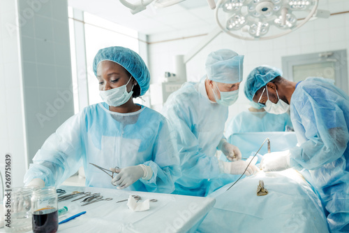 Photos nurse and team of talented doctors using cutting and dissecting instrument durin