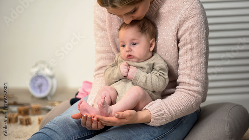Young mother admiring sons tiny legs, baby sitting on womans lap, happiness