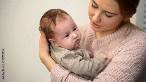 Attentive female babysitter holding little adorable baby and talking to him