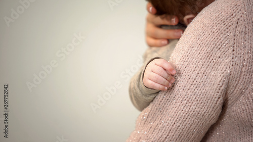 Young mother cuddling adorable infant in arms, tiny hand closeup, baby care