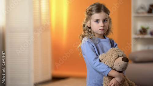 Fotografie Adorable sad little girl hugging favorite teddy bear feeling lonely in orphanage