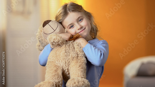 Beautiful girl with favourite teddy bear toy smiling at camera, happy childhood