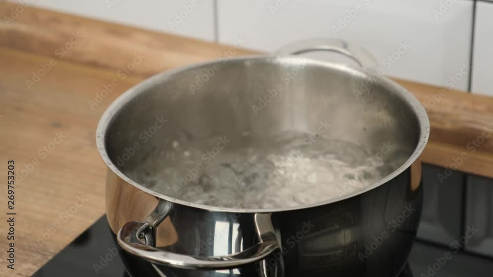 hand of woman Adding a salt to boiling water in pot on induction hob hand of woman Adding a salt to boiling water in pot on induction hob