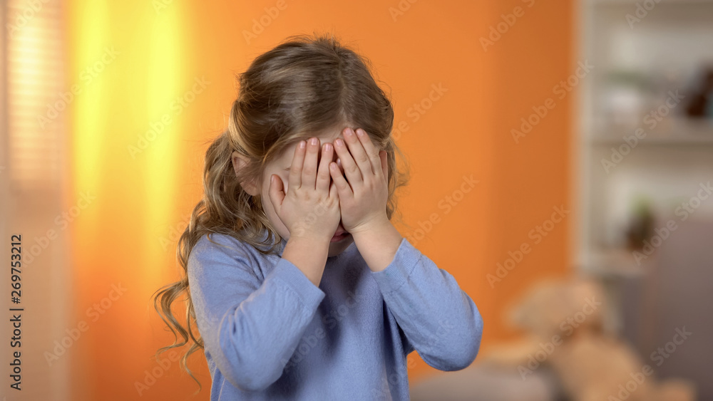 Pretty preschool girl closing eyes with hands, suffering bullying, friends lack Pretty preschool girl closing eyes with hands, suffering bullying, friends lack