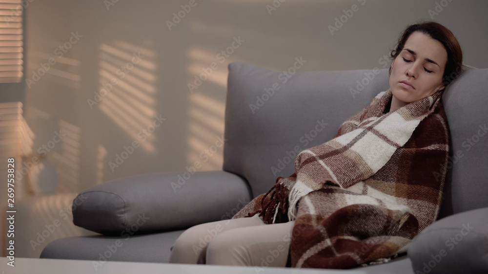 Obraz premium Lonely young depressed female sleeping on couch, covered with plaid, despair