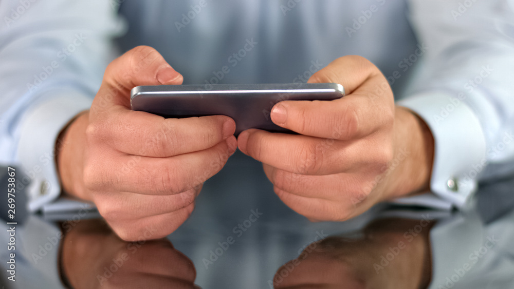 Male hands playing game on smartphone, fingers touching screen, gadget addiction Male hands playing game on smartphone, fingers touching screen, gadget addiction