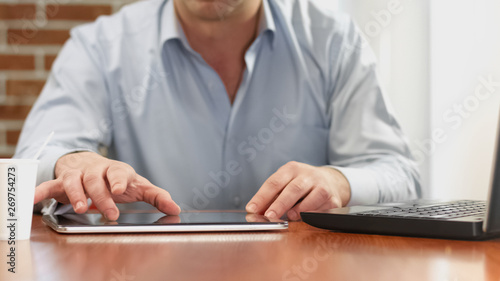 Male freelancer working project using tablet sitting at table, business app