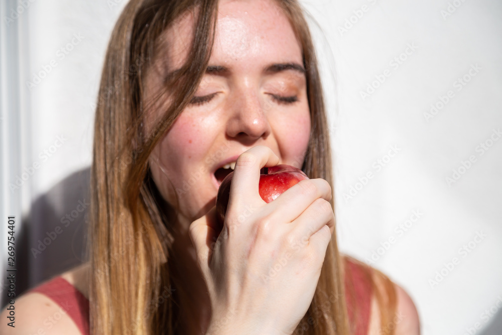 Young joyful attractive woman in casual summer dress sitting on balcony and eating tasty juicy red apple Young joyful attractive woman in casual summer dress sitting on balcony and eating tasty juicy red apple