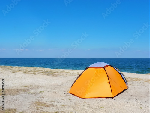 orange tent on the sand against the background of the sea and sky