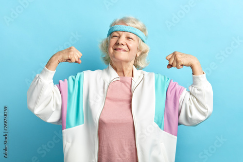 Happy, proud elderly attractive woman flexing both arms in the air with fists pressed showing strength or success, celebrating sport achievements.