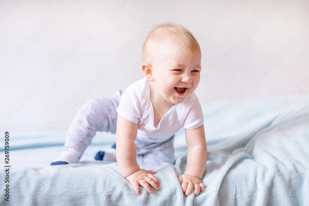 Adorable baby boy in white sunny bedroom. Newborn child relaxing on a blue bed. Nursery for young children. Newborn kid during tummy time with toys at a window - obrazy, fototapety, plakaty 