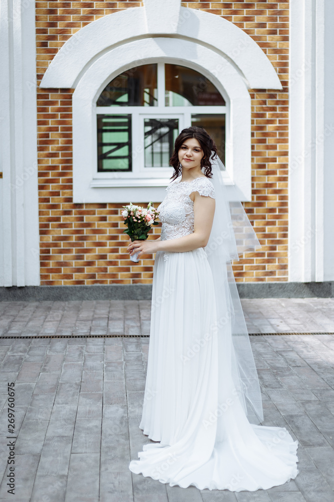Happry romantic bride in white long dress with bouquet in hands smiles and looks at camera near clock tower in city center Happry romantic bride in white long dress with bouquet in hands smiles and looks at camera near clock tower in city center