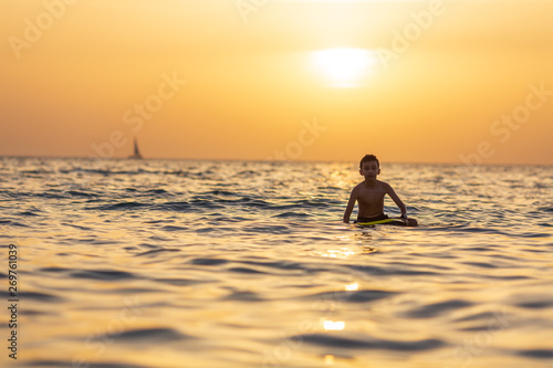 Silhouette of a boy floating on the sea with surfboard on the excellent background of orange sunset