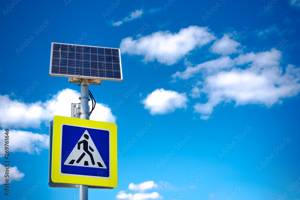 Bright blue and yellow pedestrian crosswalk sign with traffic warning. Powered by solar energy with its own solar panel Bright blue and yellow pedestrian crosswalk sign with traffic warning. Powered by solar energy with its own solar panel