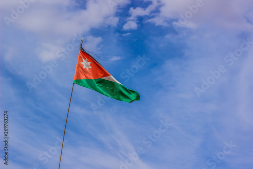 Jordanian flag evolving in the wind on blue sky with white clouds background 