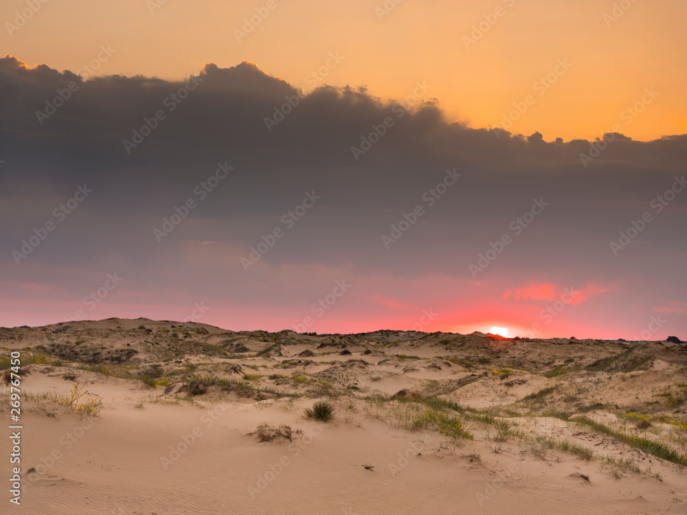 Sun under dark clouds above sand desert