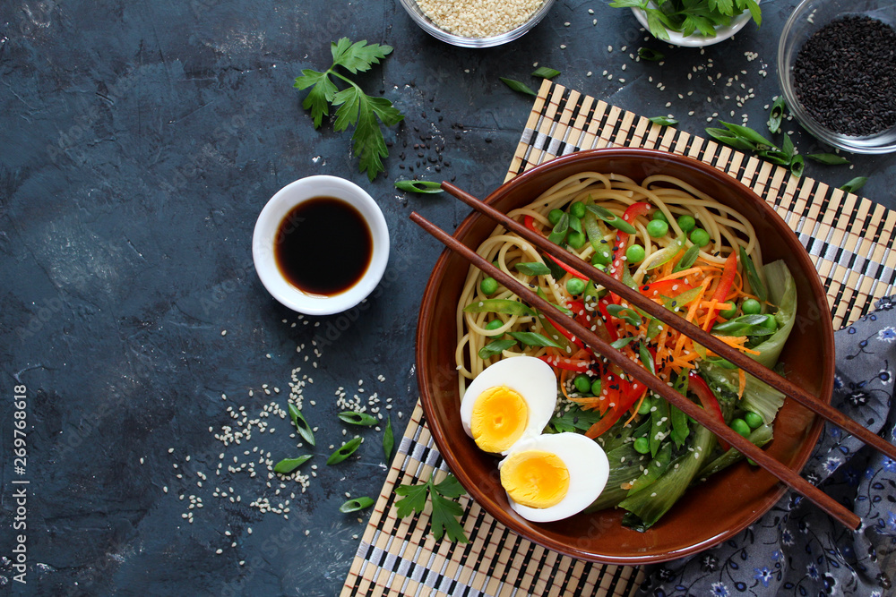 Noodles with vegetables and eggs in bowl on dark background. Top view with copy space. Asian food.