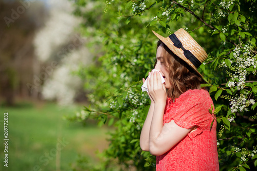 Fotografie Young girl blowing nose and sneezing in tissue in front of blooming tree