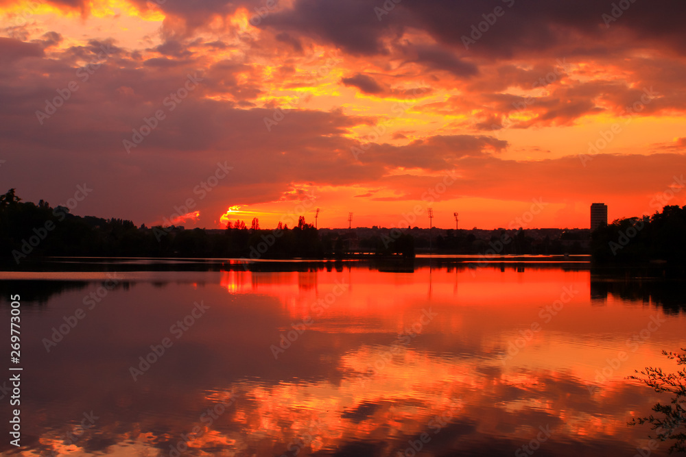 Golden sunset on the water with symmetry of colorful clouds cumulonimbus. Beautiful reflection of the sun's rays in a lake. Isolated tower on the skyline