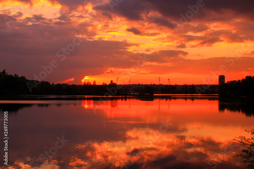 Golden sunset on the water with symmetry of colorful clouds cumulonimbus. Beautiful reflection of the sun's rays in a lake. Isolated tower on the skyline