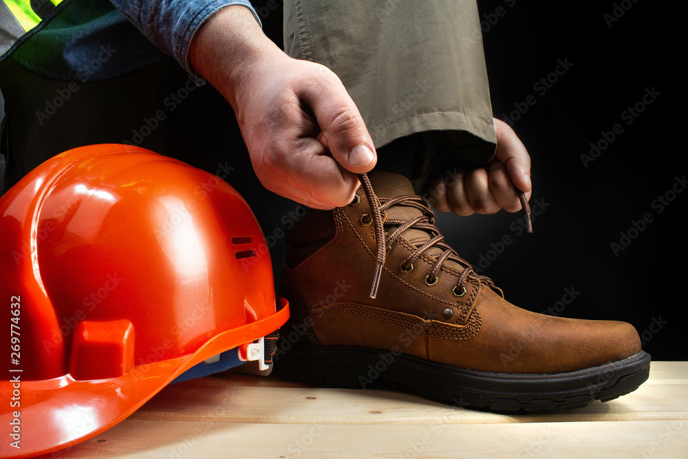 Worker with helmet lacing up leather boots. - obrazy, fototapety, plakaty 