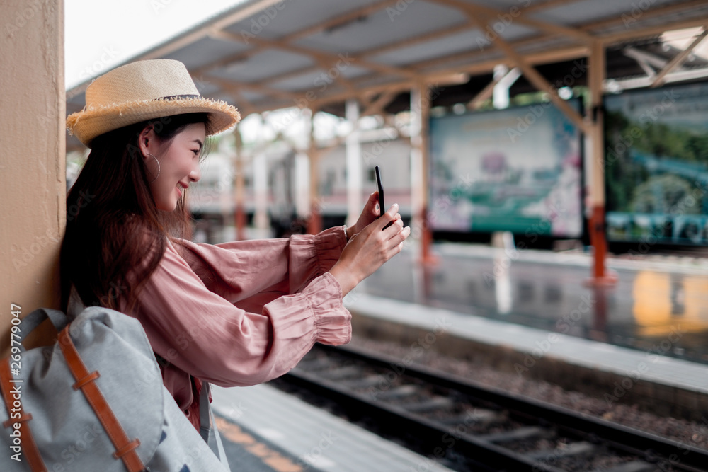 Smiling woman traveler with backpack holding smartphone on holiday relaxation at the train station,relaxation concept, travel concept
