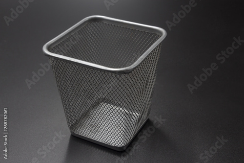 Silver-gray square metal paper basket for office is placed quietly on a black background.